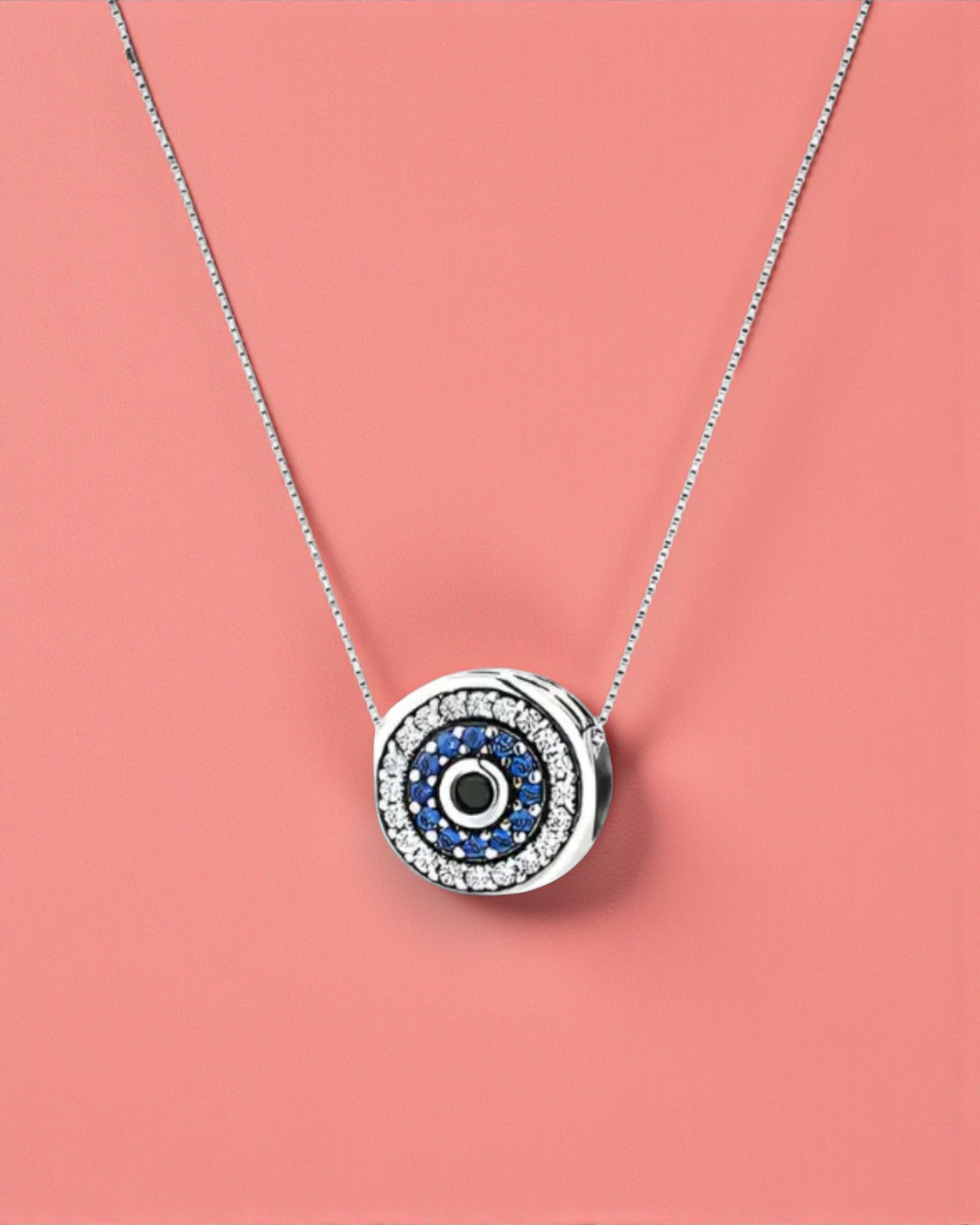 Silver necklace with a round pendant featuring blue and black stones on a pink background