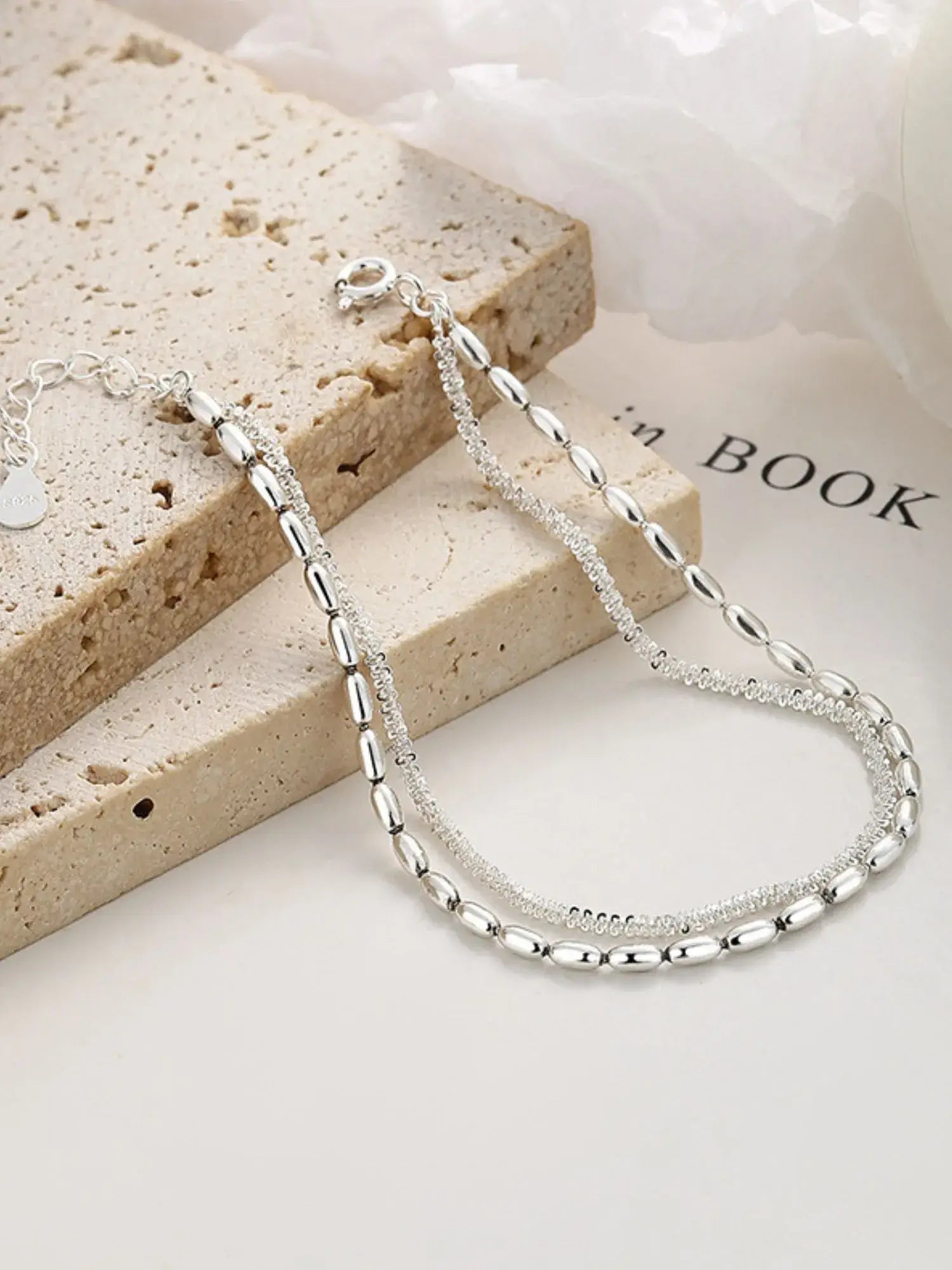 Silver necklace on a textured surface with a book in the background