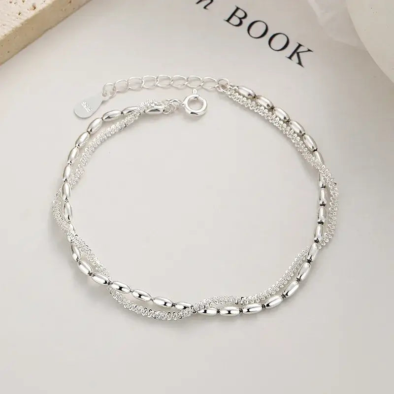 Silver bracelet on a light gray surface with 'BOOK' text in the background