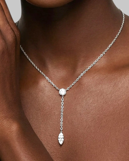 Silver necklace with a pendant on a person's neck against a neutral background