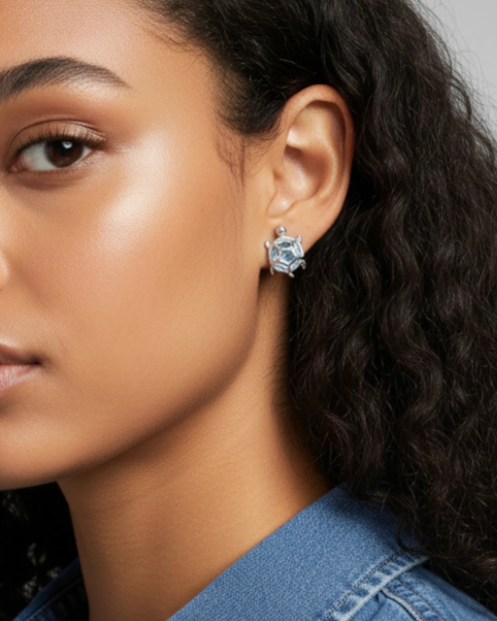 Close-up of a model wearing Sea Turtles Stud Earrings in Silver with aquatic blue glass stone.