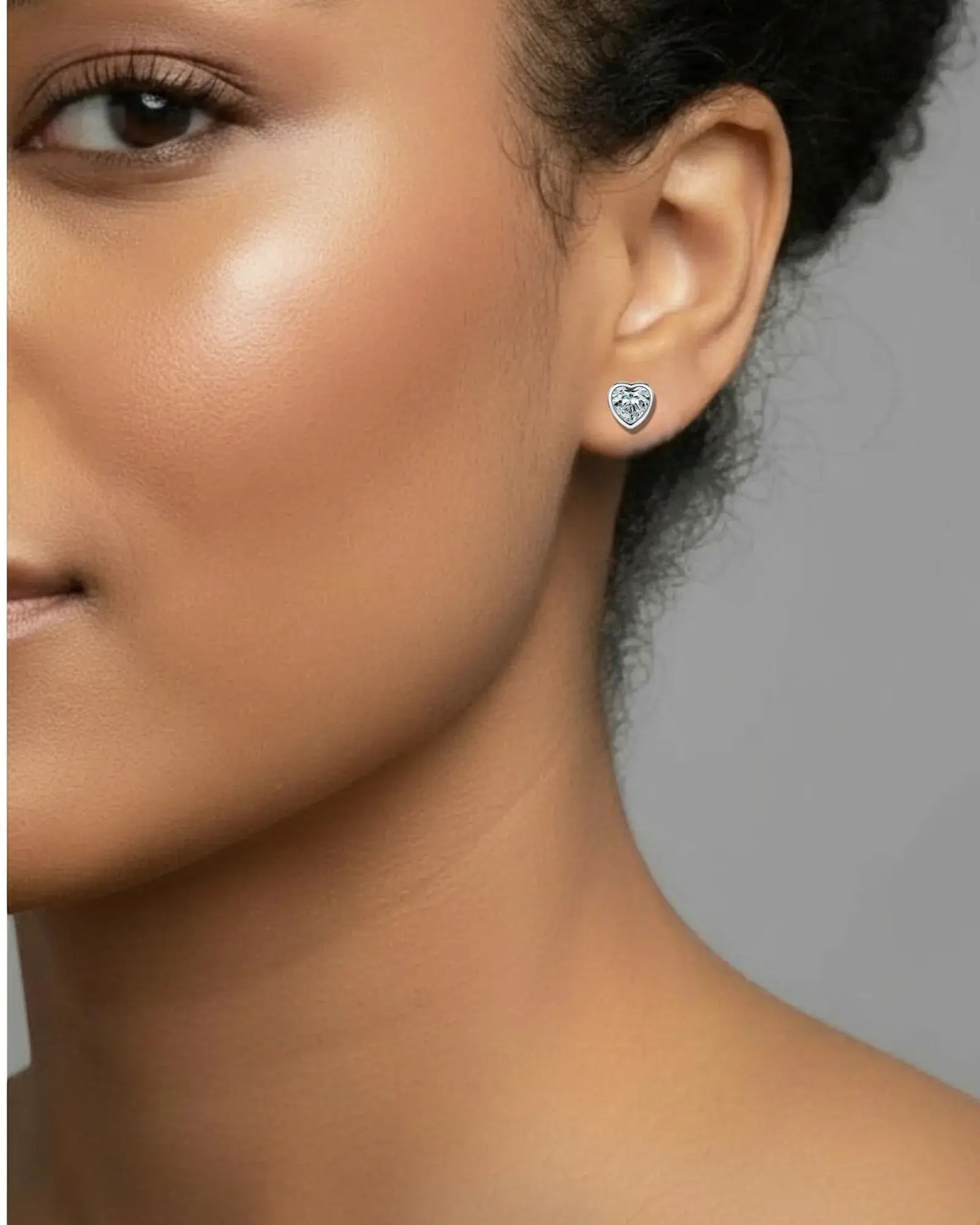Close-up of a person wearing a heart-shaped earring with a gray background