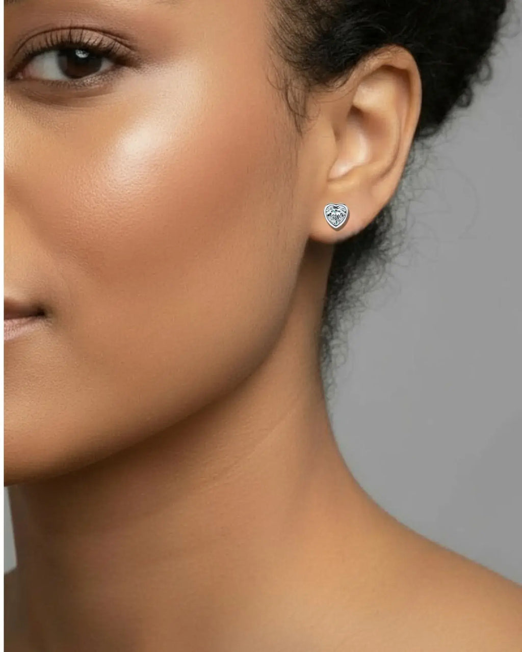 Close-up of a person wearing a heart-shaped earring with a gray background