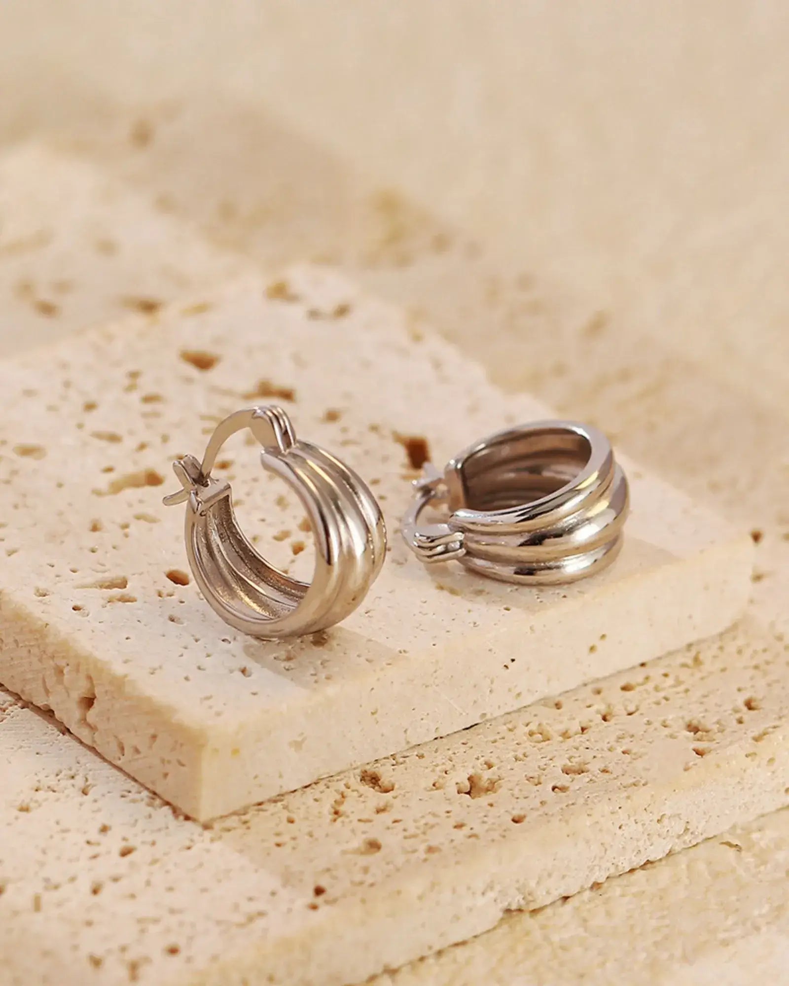 Aura Curve Hoop Earrings on a textured surface, showcasing their sleek, sculptural design in polished silver.