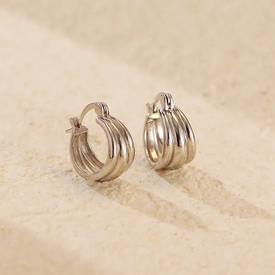 Aura Curve Hoop Earrings in polished silver, showcasing sleek design with wave-like curves and geometric silhouette.