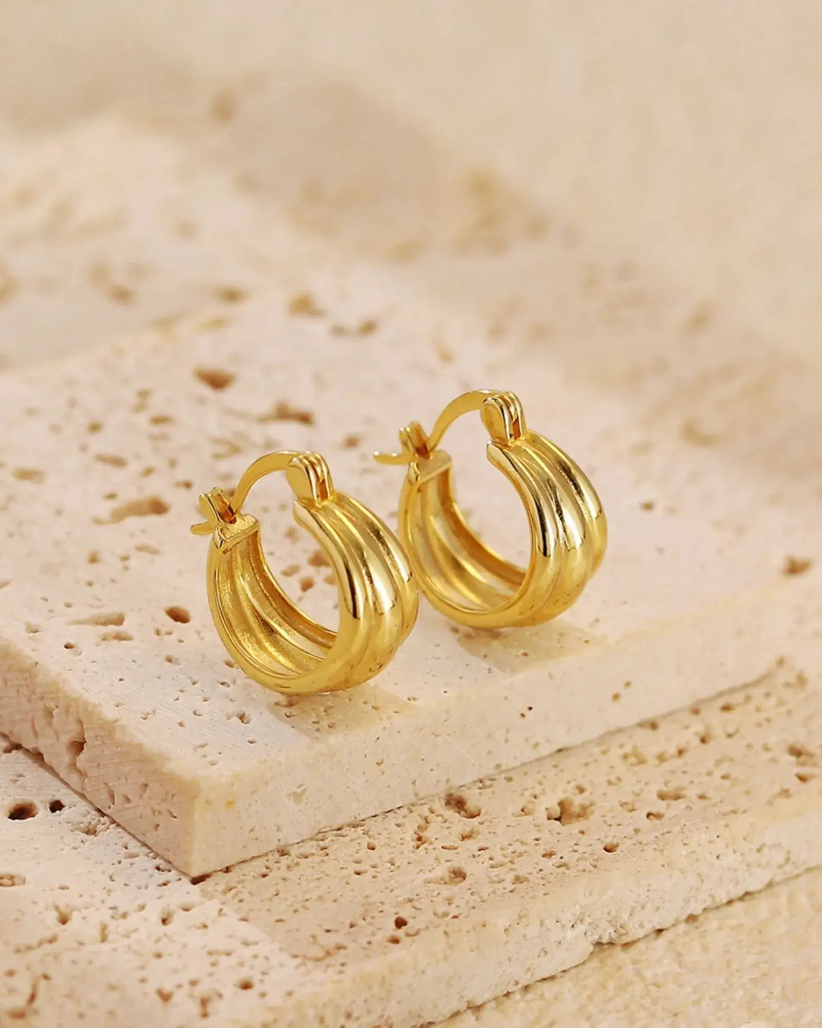 Aura Curve Hoop Earrings in gold, featuring soft wave-like curves and a sculptural design, set on natural stone.