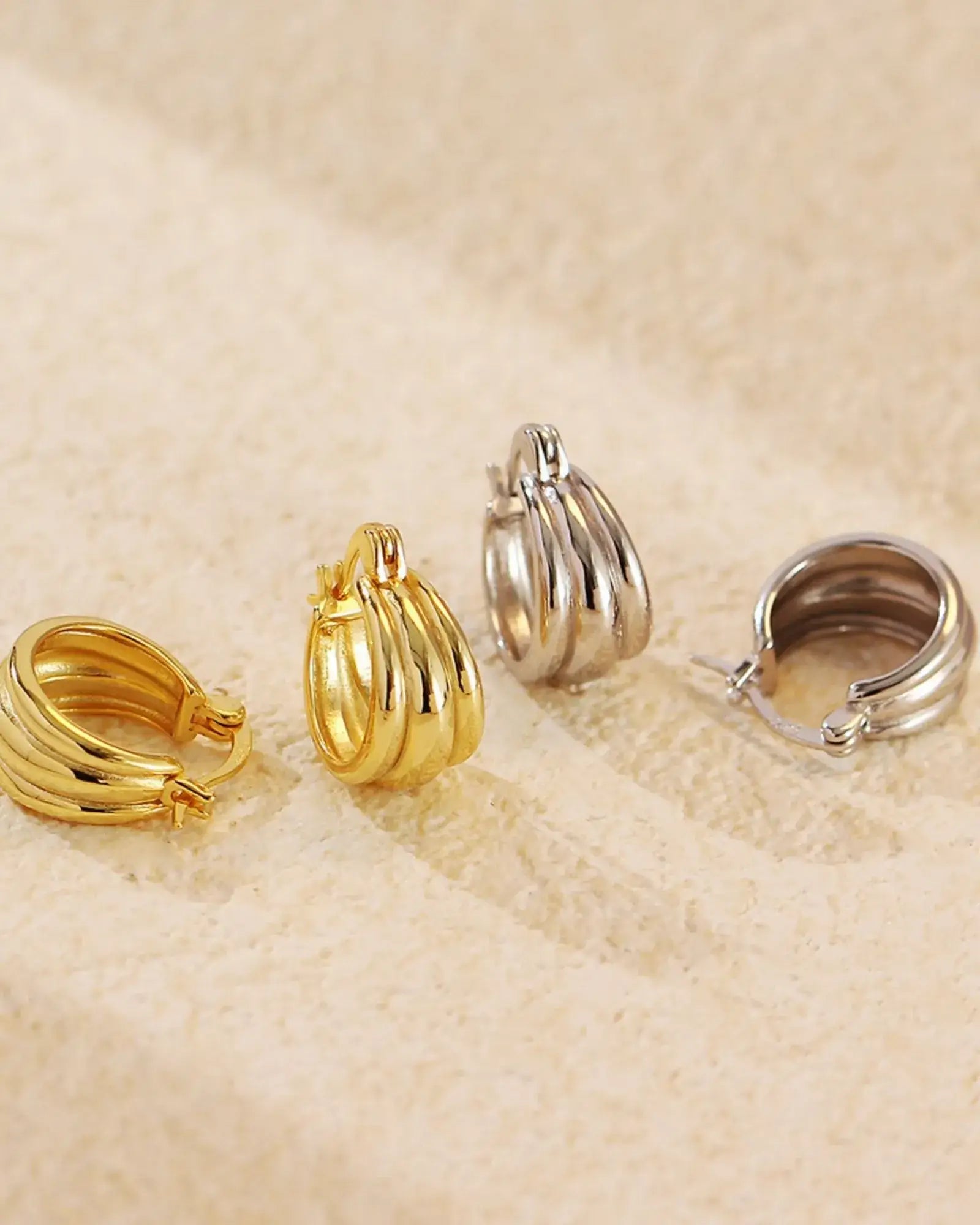 Aura Curve Hoop Earrings in gold and silver finishes showcasing sleek, sculptural design with soft, wave-like curves.