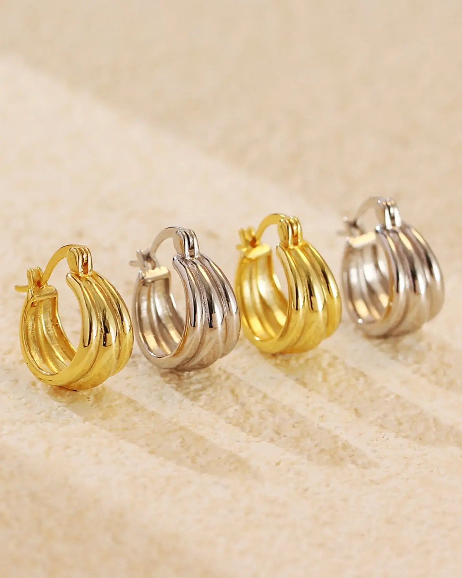 Aura Curve Hoop Earrings in gold and silver finishes showcasing sculptural wave-like design.