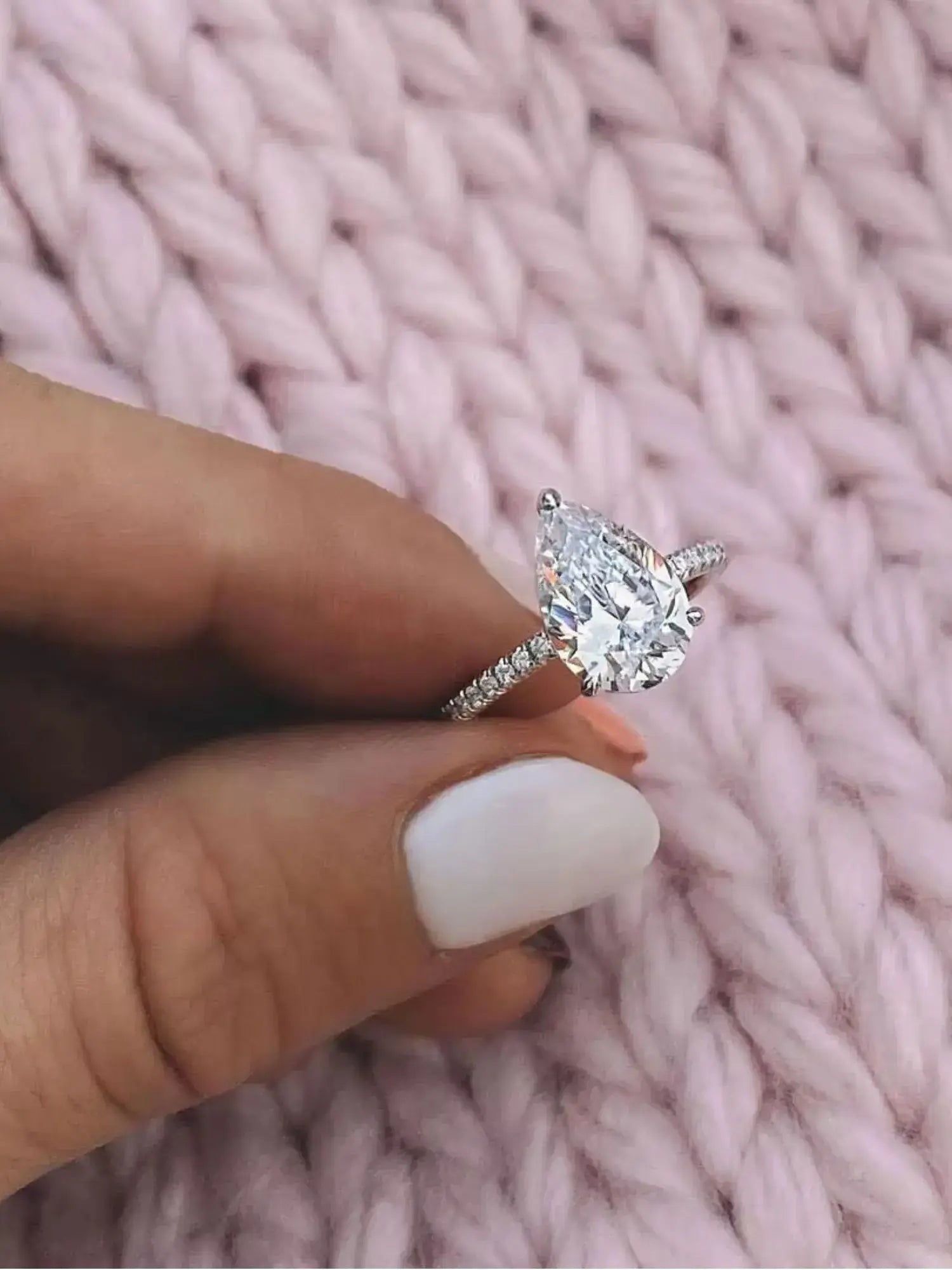 Golden Promise Engagement Ring with water drop-shaped cubic zirconia in sterling silver, showcased on a knitted pink background.