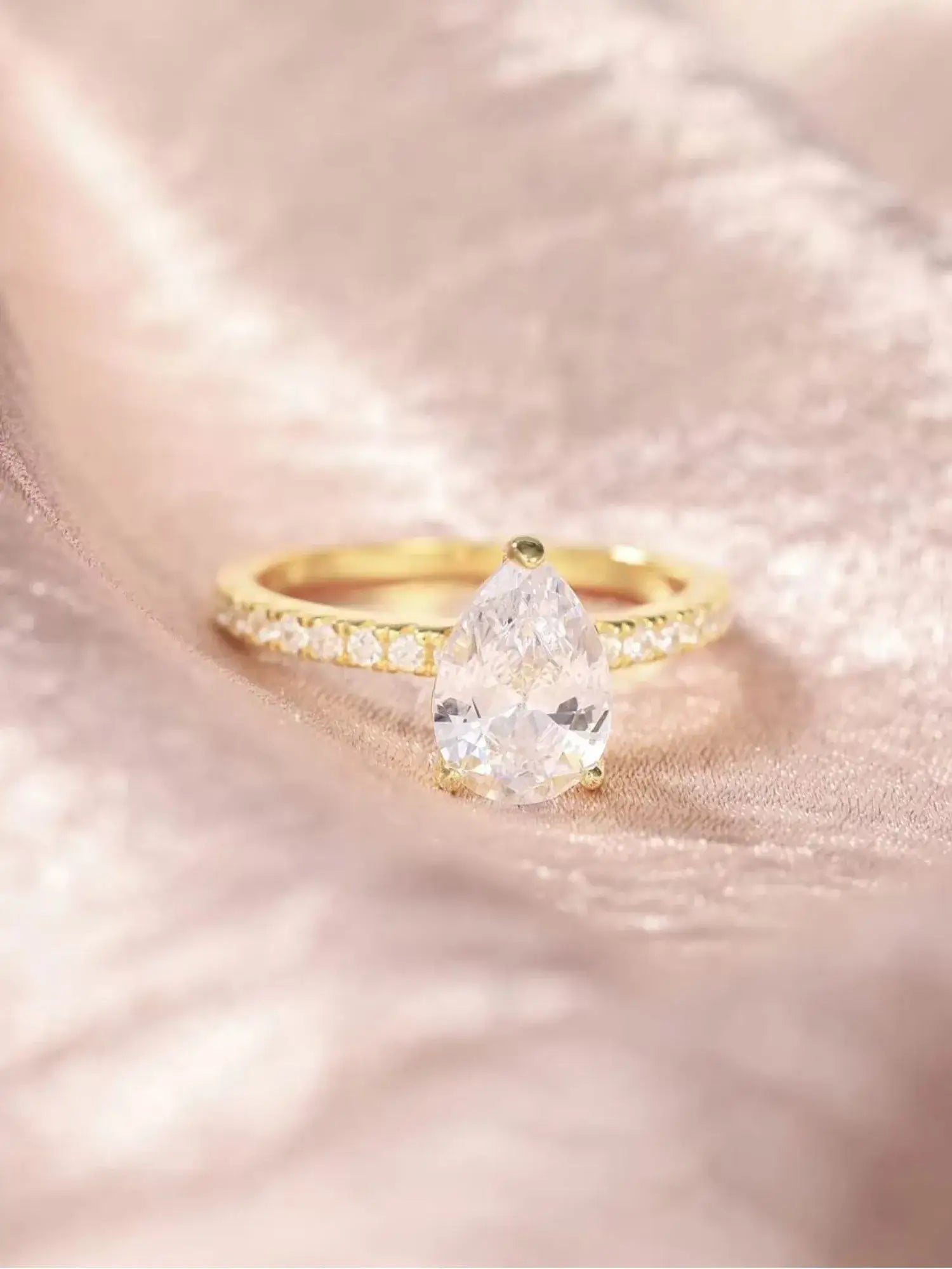 Golden Promise Engagement Ring with pear-shaped cubic zirconia on a gold band, set against soft fabric.