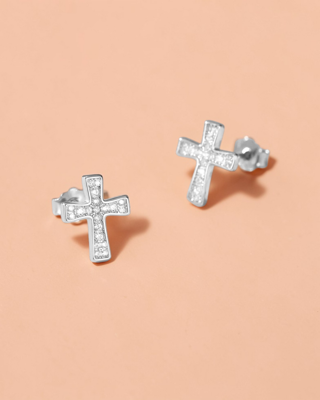 0.1 Ct Moissanite Cross Stud silver earrings with brilliant sparkle on a soft peach background.