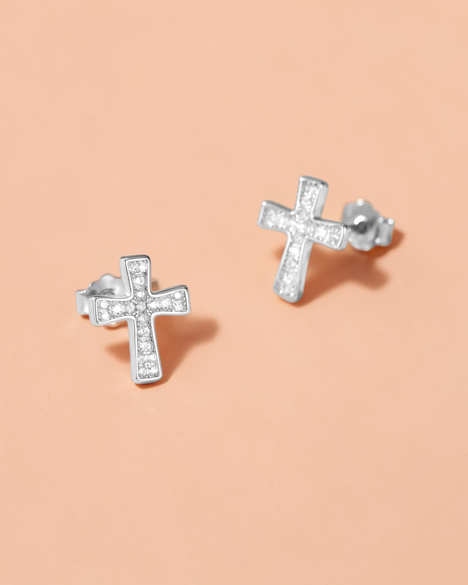 0.1 Ct Moissanite Cross Stud silver earrings with brilliant sparkle on a soft peach background.