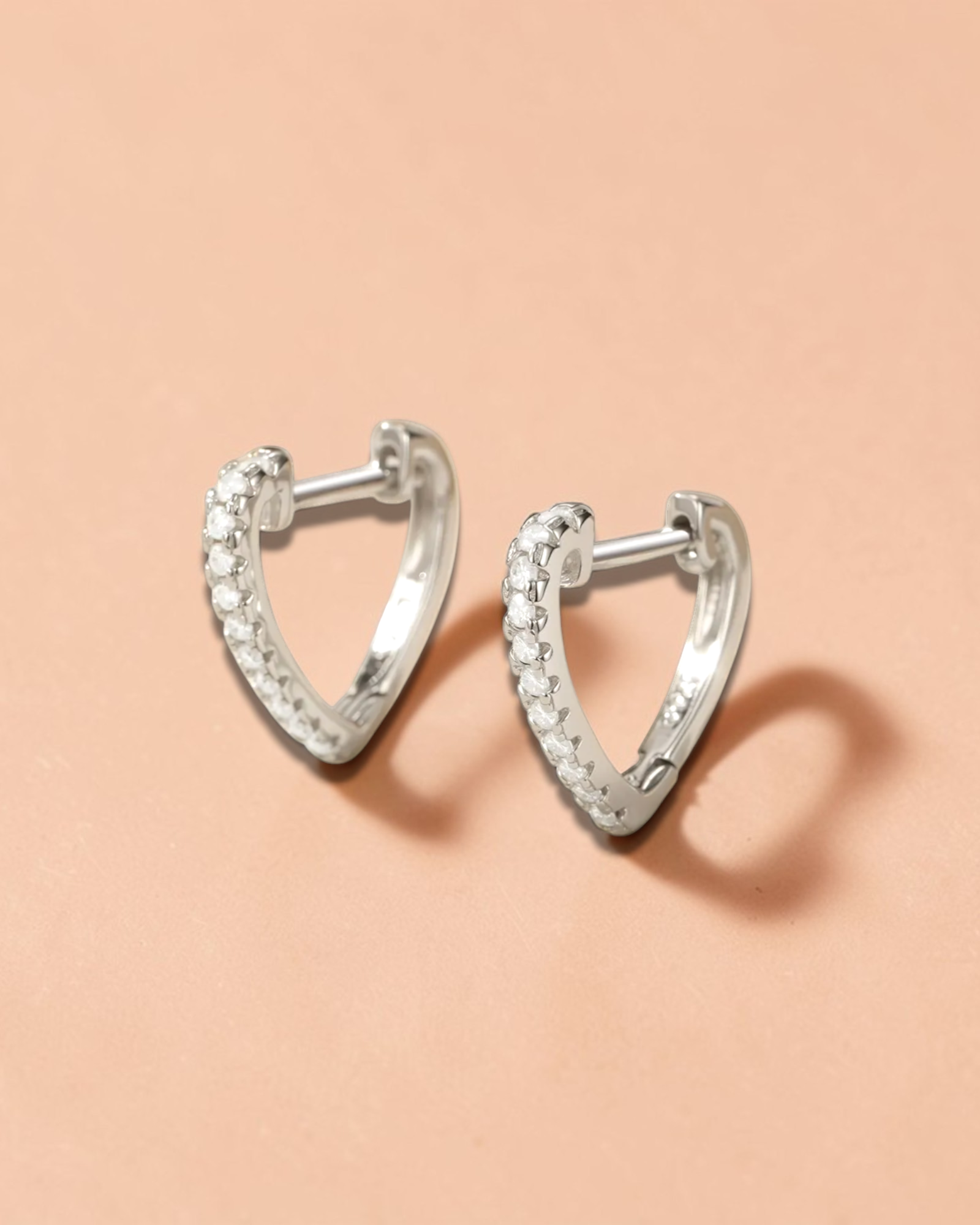 0.2 Ct Moissanite Heart shaped hoops showcasing brilliant sparkle on a soft peach background.