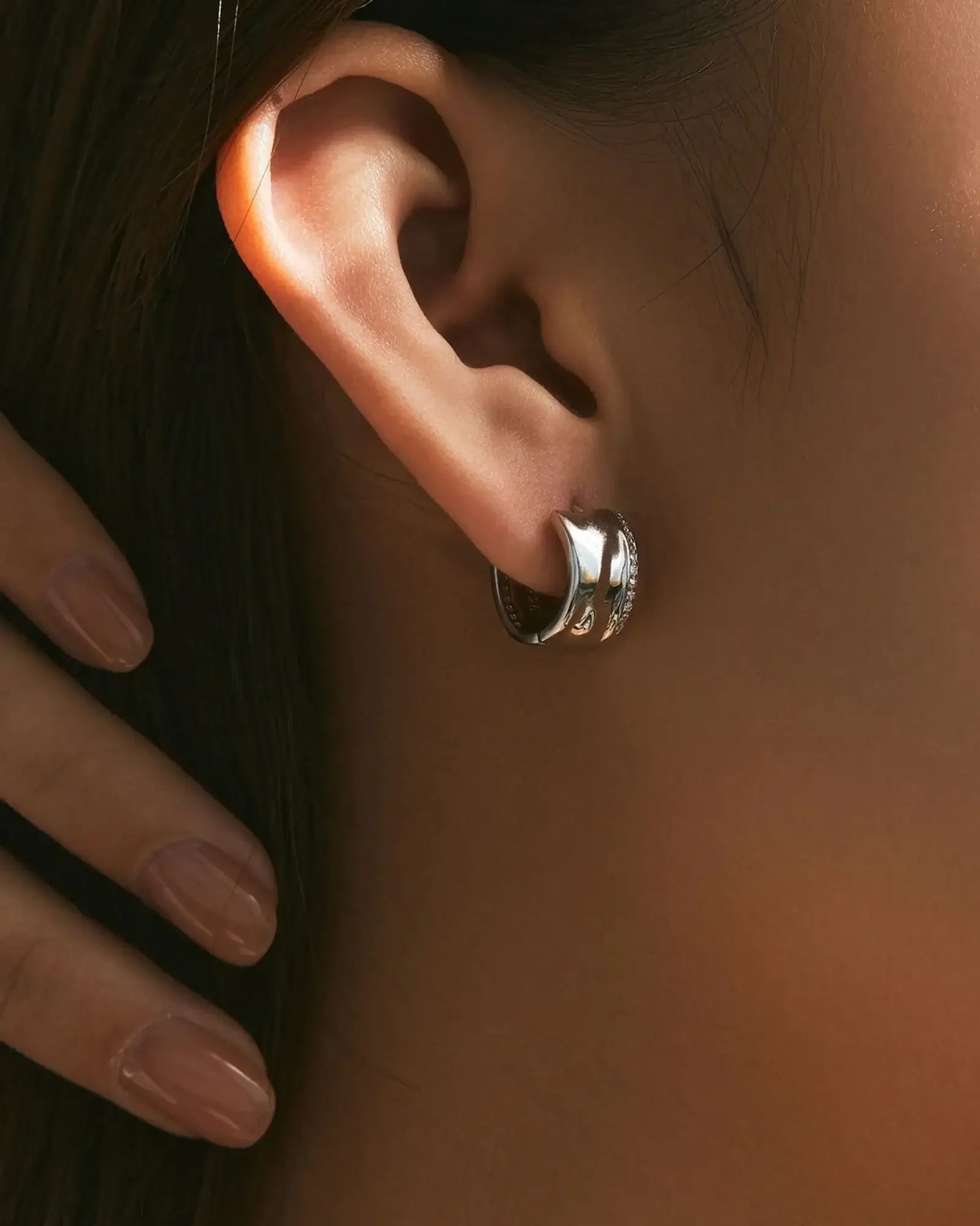 Irregular small zircon hoop earrings on a model's ear, showcasing elegant design and rhodium-plated finish.