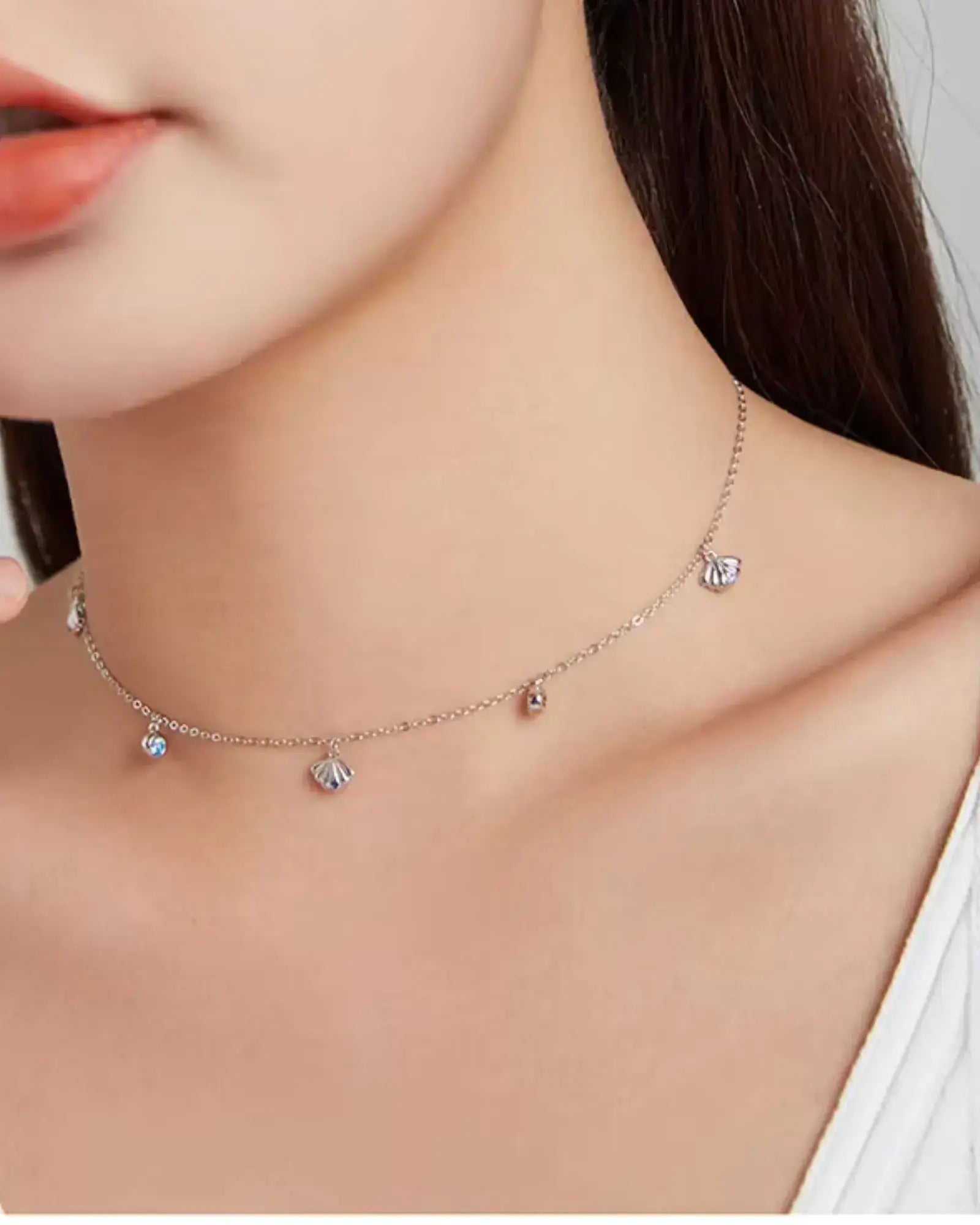 Elegant scallop charm necklace in silver with colorful blue zircon, showcased on a model's neck.