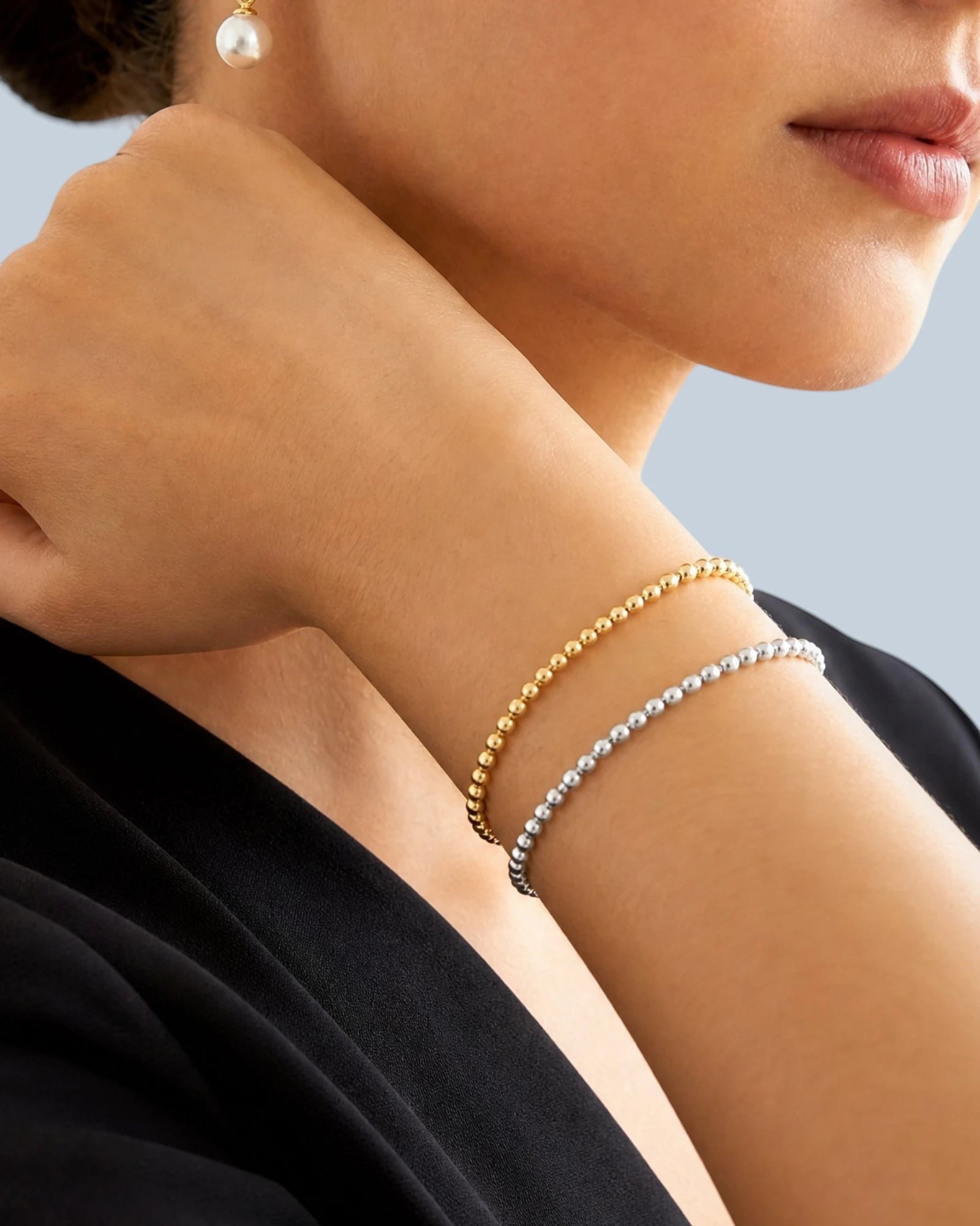 Pearlystones gold-tone and silver-tone beaded chain bracelets worn on a woman's wrist. Delicate, uniform beads add shimmer.