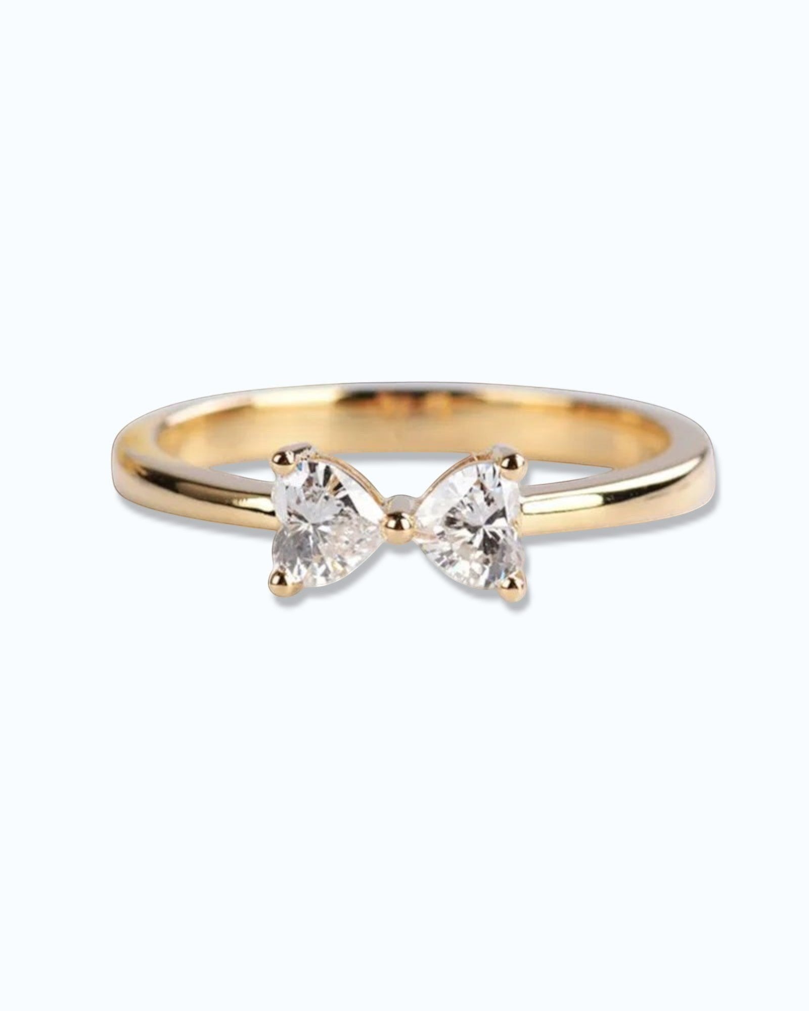 Pearlystones gold ring with a delicate bow design adorned with two heart-shaped clear gemstones.