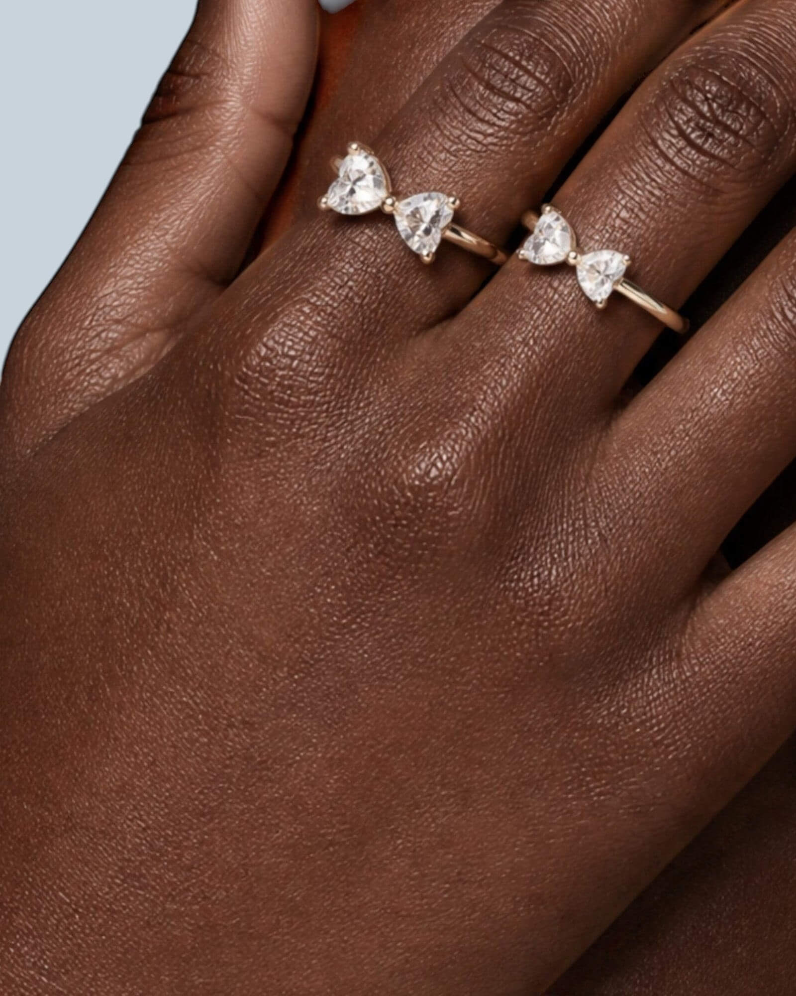 Pearlystones delicate gold bow ring with two heart-shaped gemstones on a model's hand.
