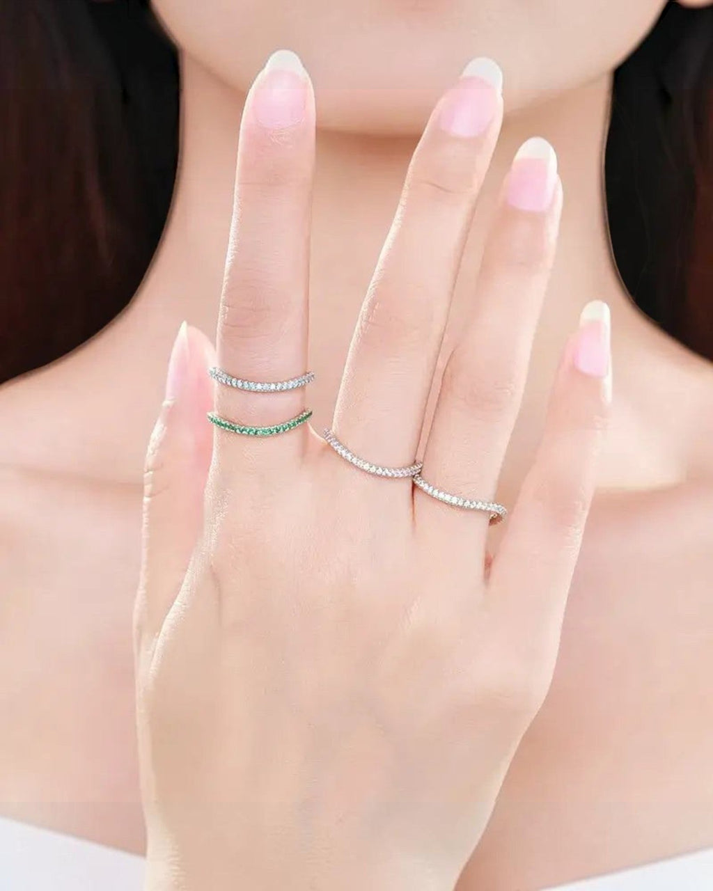Pearlystones delicate eternity band ring with emerald-green stones on a silver band, worn stacked on fingers.