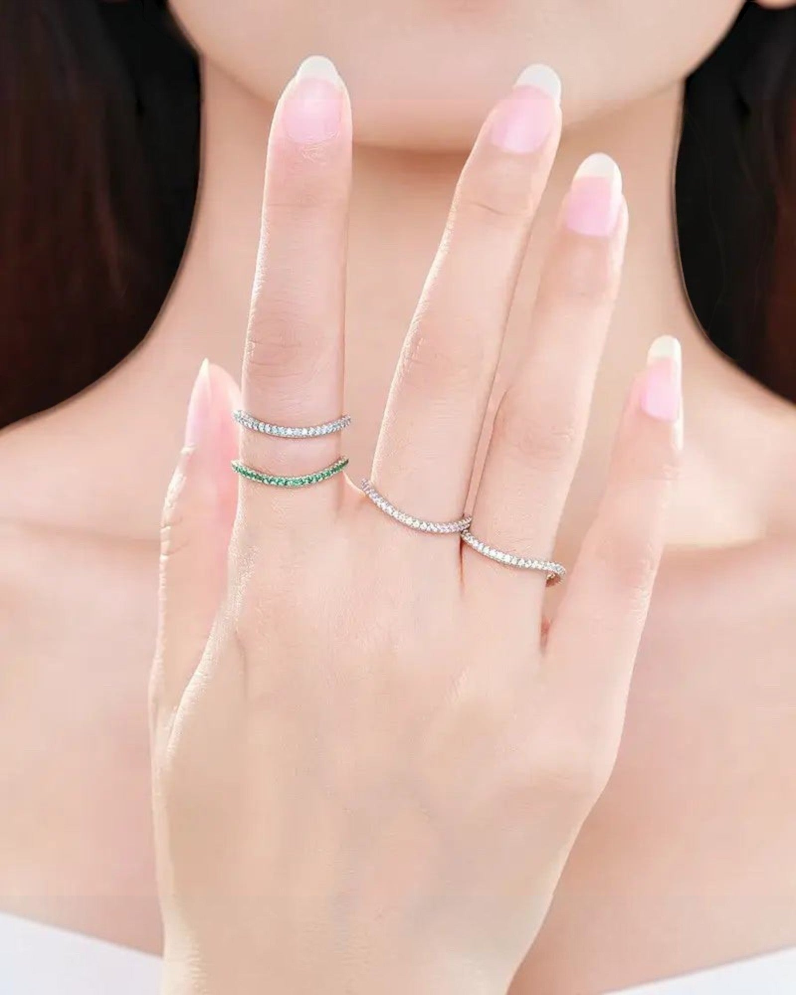 Pearlystones delicate eternity band ring with emerald-green stones on a silver band, worn stacked on fingers.