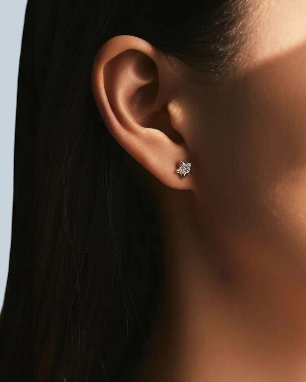 Close-up of an ear wearing a diamond earring with a blurred background