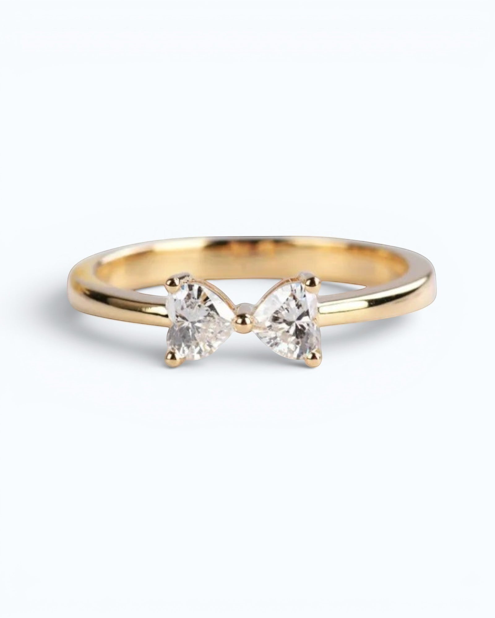 Pearlystones gold ring with a bow design featuring two heart-shaped clear gemstones.