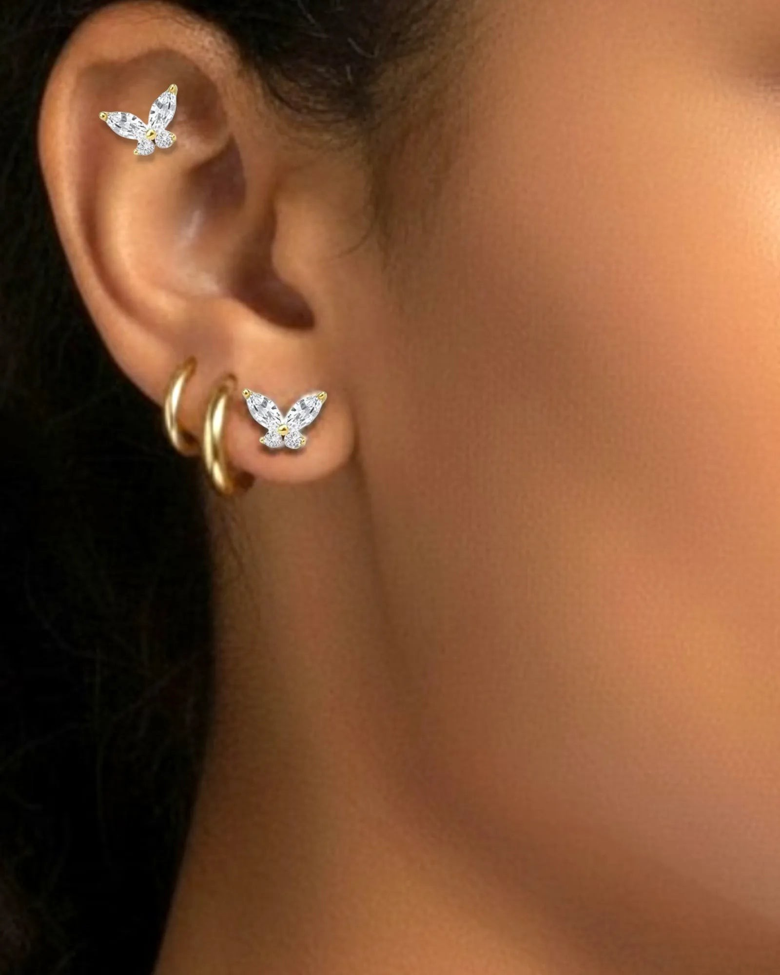 Pearlystones butterfly cartilage stud in gold with zircon stones worn on a model's ear with matching gold hoops.