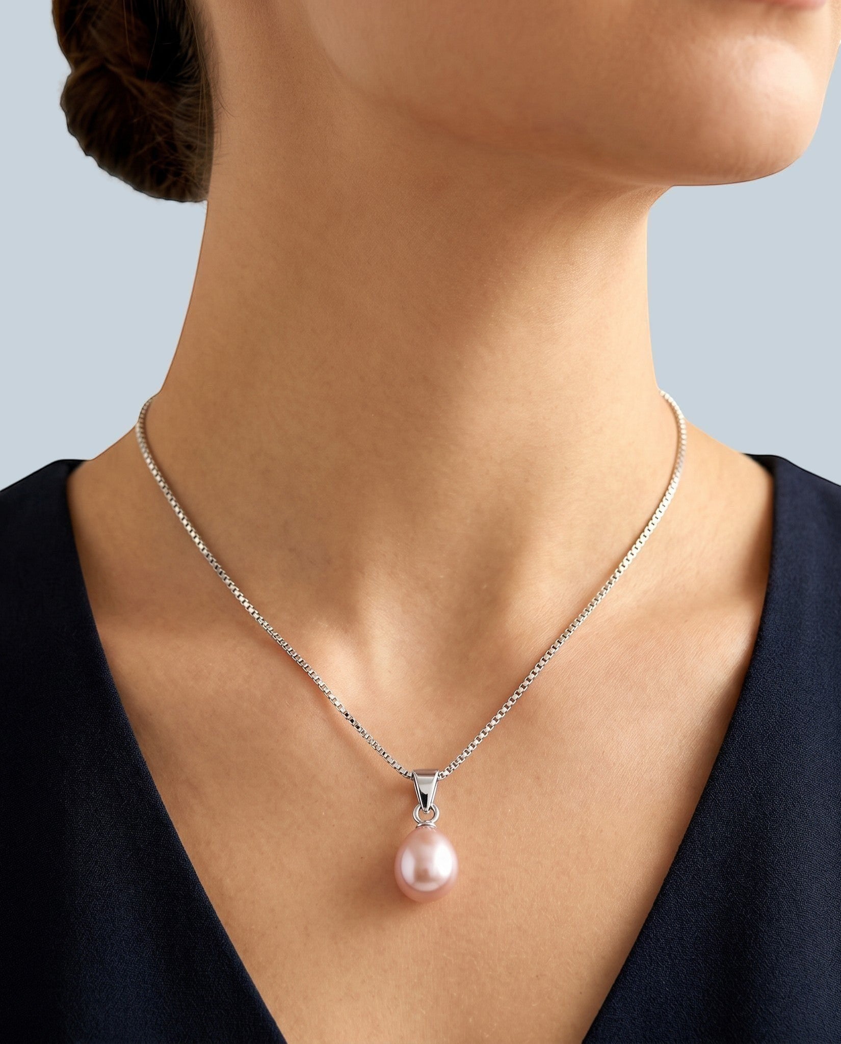 Pearlystones teardrop pink pearl pendant on a delicate silver-tone box chain worn around a woman's neck