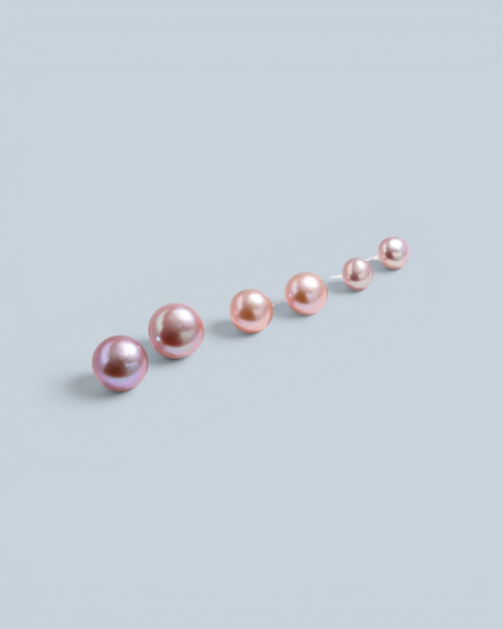Pearlystones classic round purple pearl stud earrings in graduated sizes arranged on a light grey background.