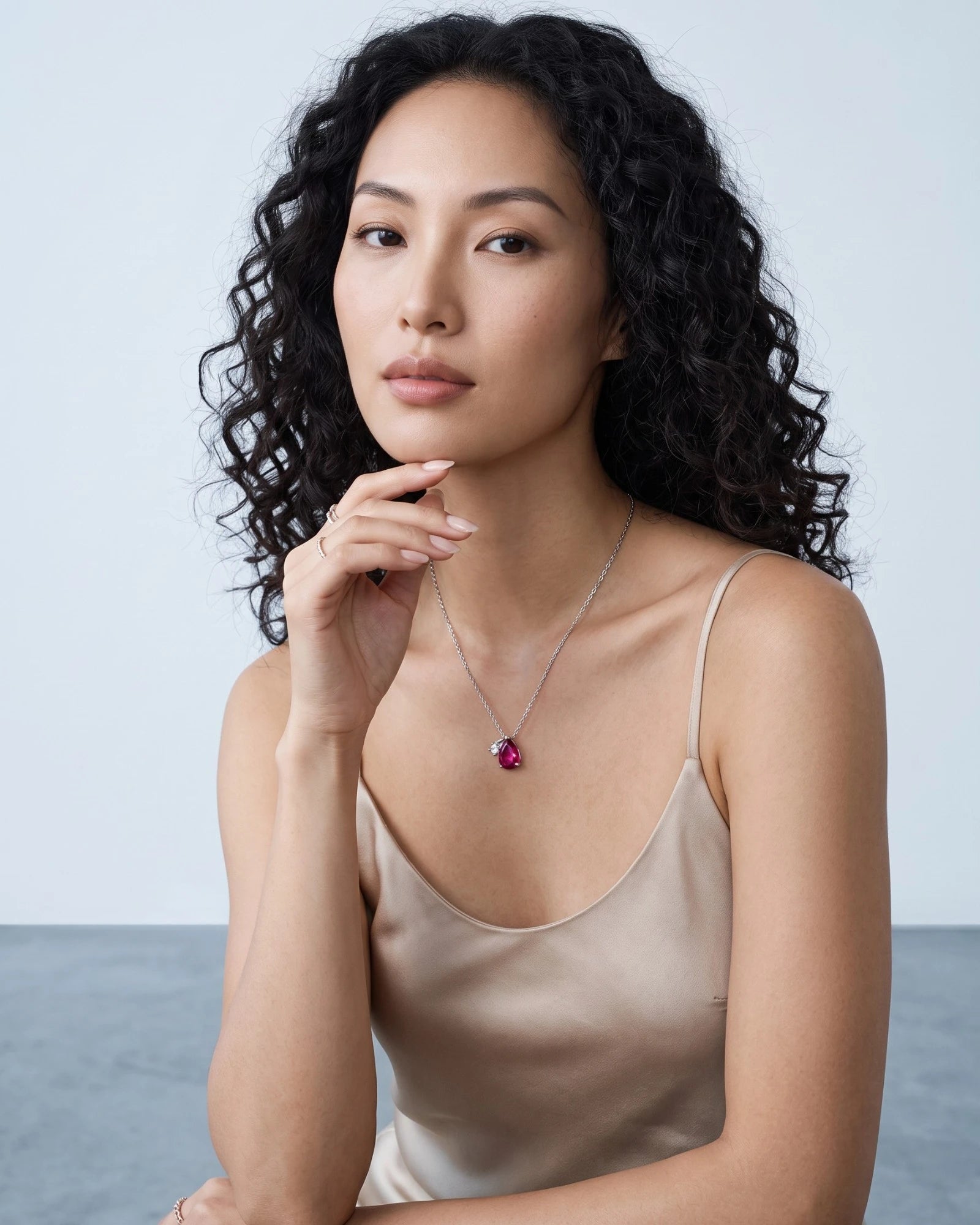 Pearlystones ruby red water droplet zircon necklace worn by a woman with curly hair in a champagne silk camisole.