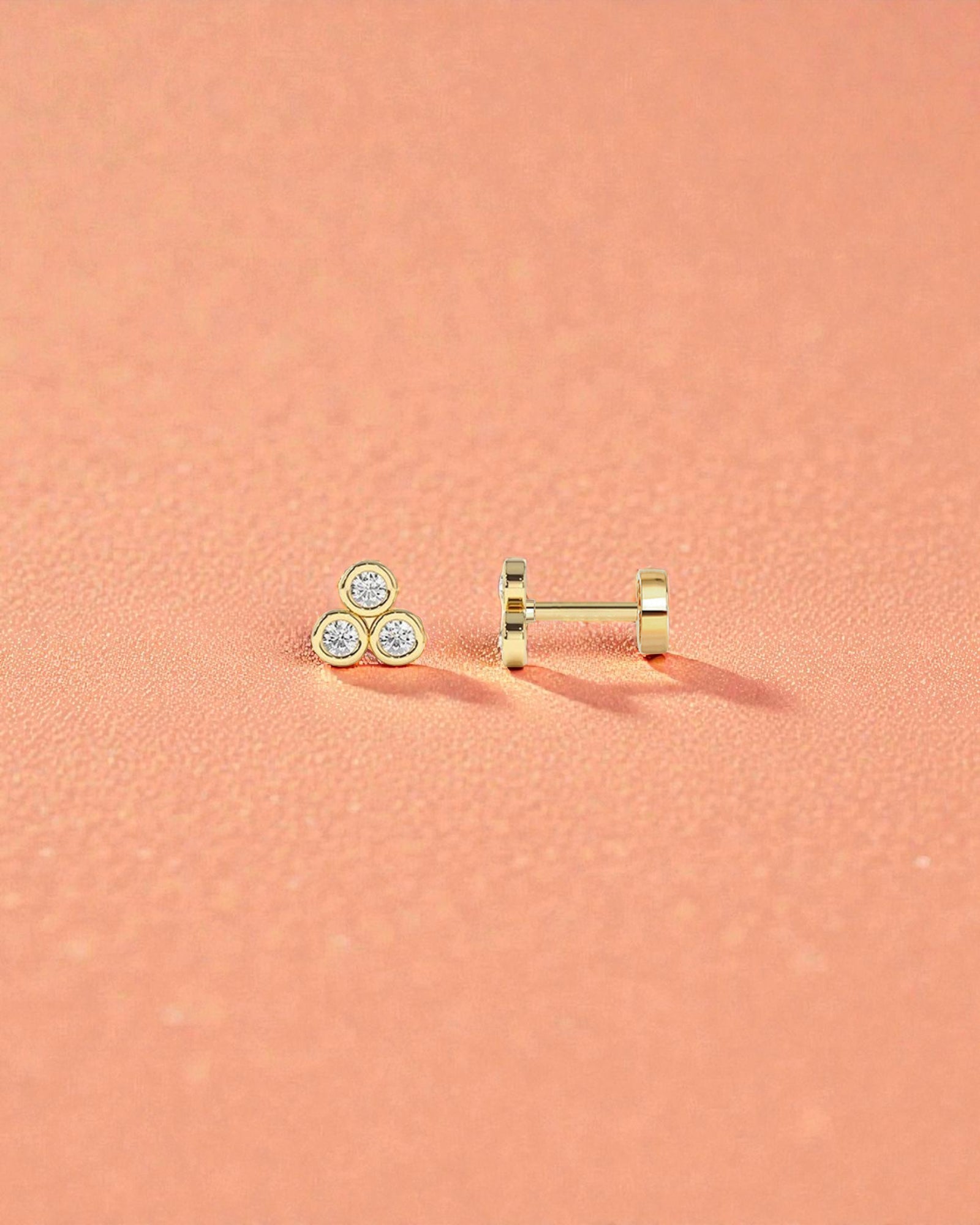 Pearlystones gold three stone cubic zirconia flat back stud earring for cartilage piercings on a peach background.