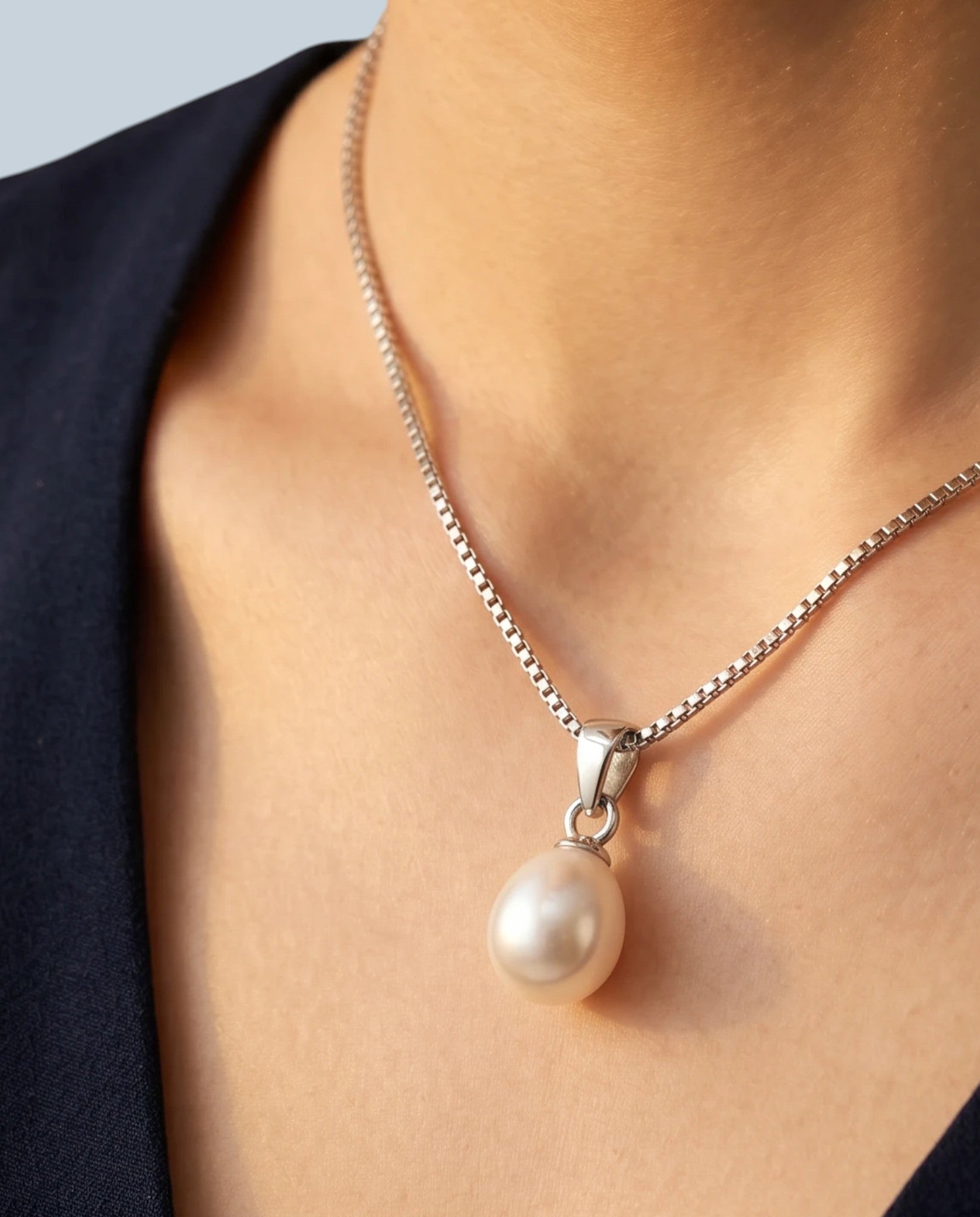 Pearlystones white teardrop pearl pendant on a rhodium plated silver box chain worn around a woman's neck
