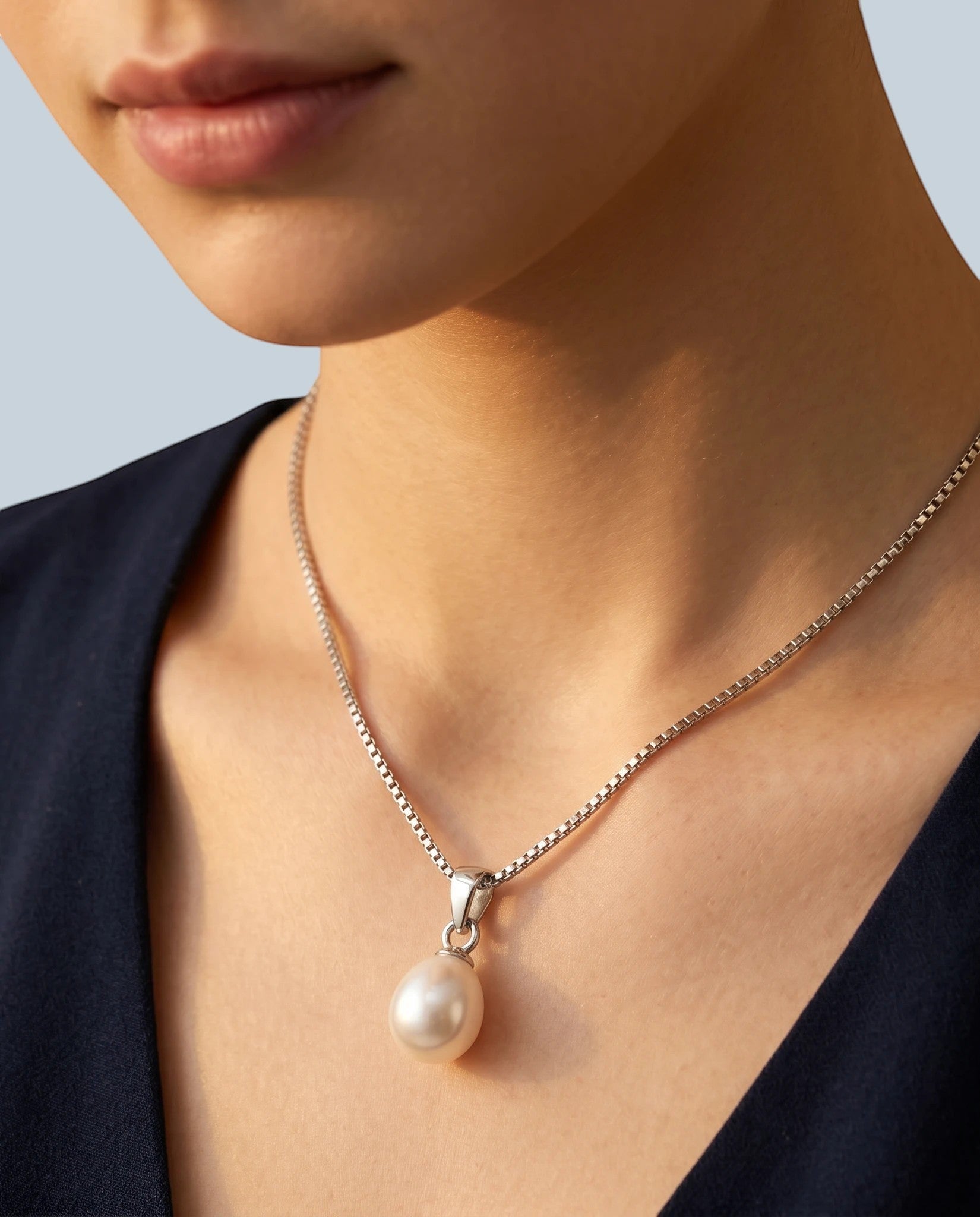 Pearlystones white teardrop pearl pendant on a rhodium plated silver box chain worn by a woman