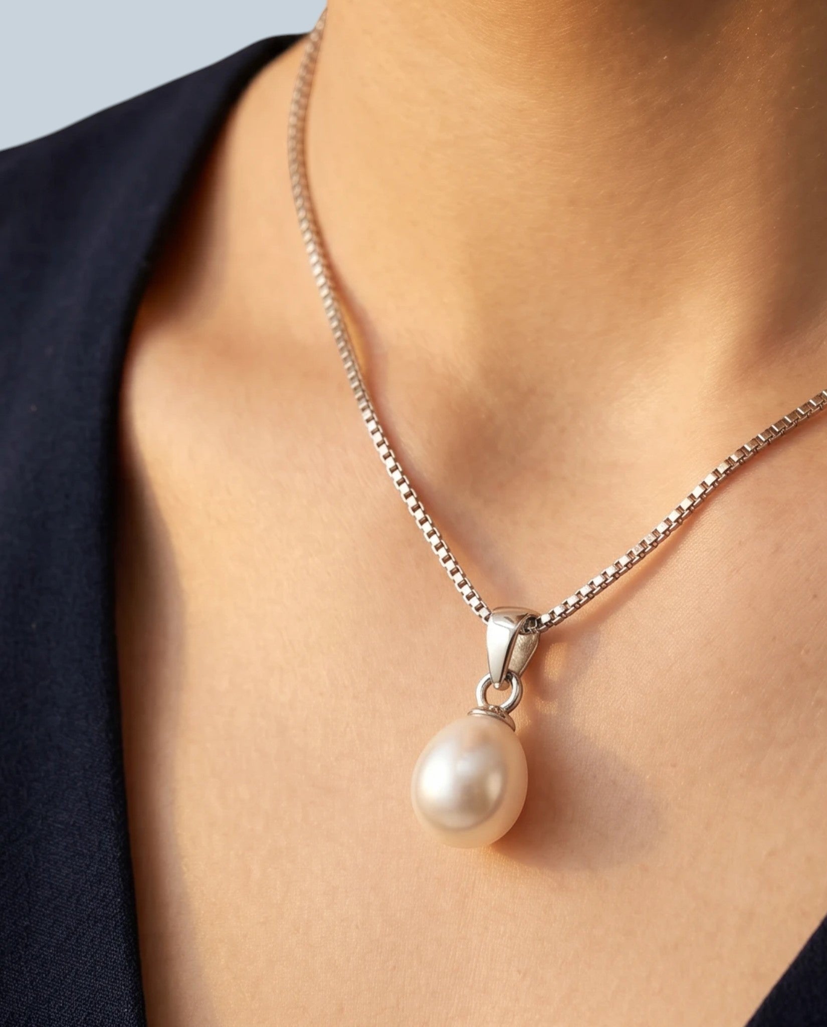Pearlystones white teardrop pearl pendant on a rhodium plated silver box chain worn around a woman's neck