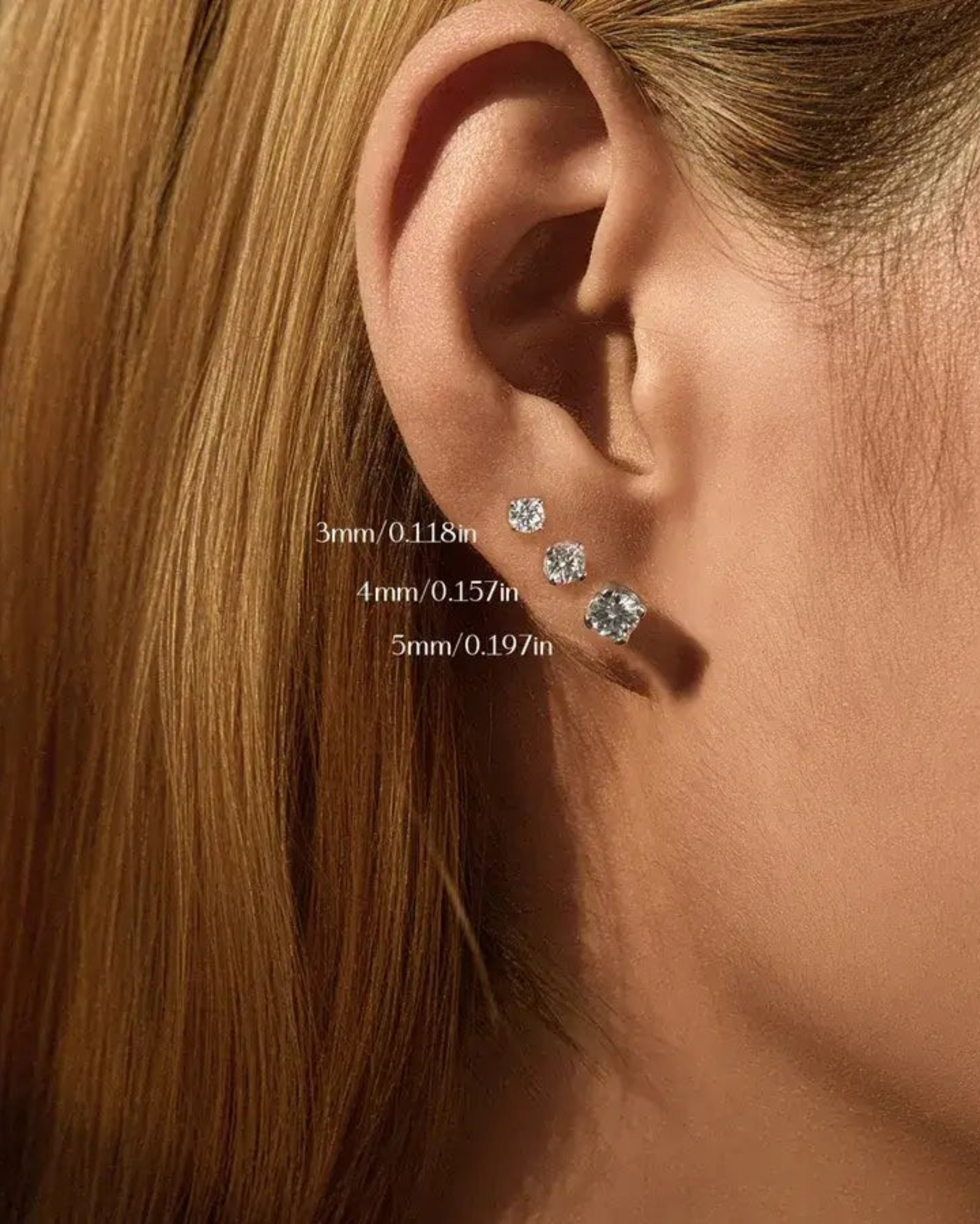 Close-up of a model's ear with three sizes of earrings: 3mm, 4mm Round brilliant cut moissanite studs, and 5mm.