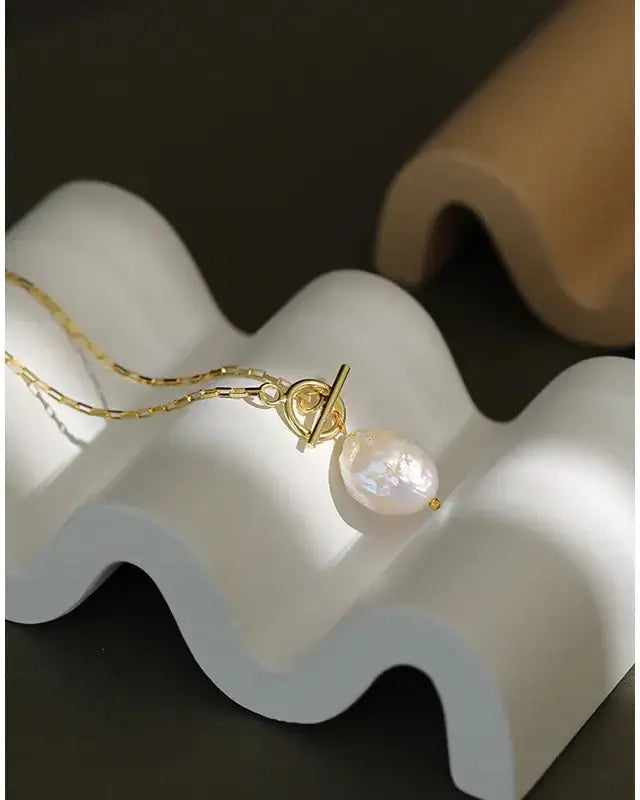 Elegant Lia Pearl Pendant Necklace on a textured surface, showcasing its lustrous pearl and gold accents.
