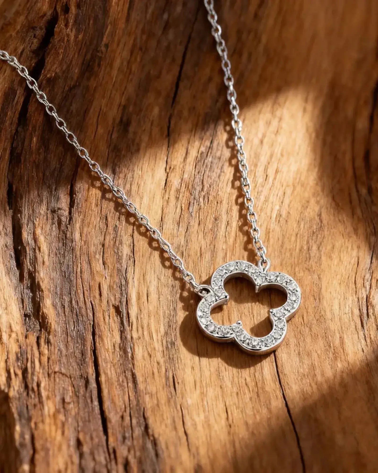 925 sterling silver clover pendant necklace on a wooden surface with sunlight.