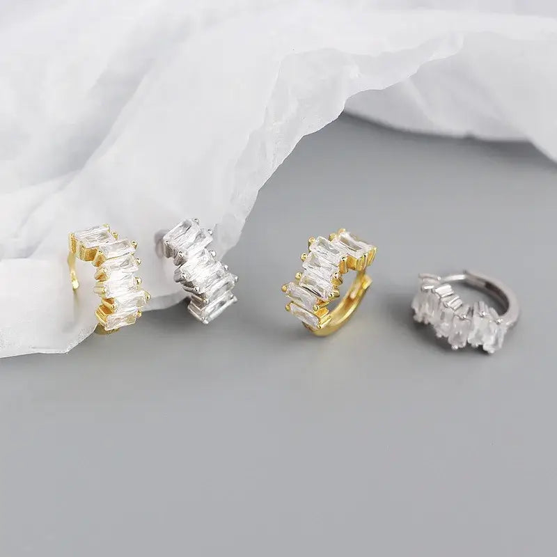 Sparkly hoops in sterling silver and 18k gold options, featuring durable white gold plating, showcased on soft fabric.