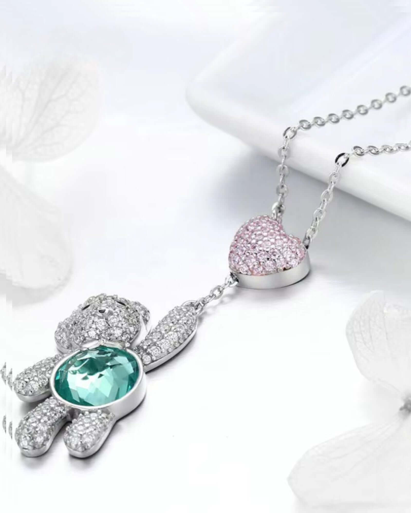 Sterling silver teddy bear pendant necklace with pink CZ heart and aqua-green stone, showcasing playful elegance.