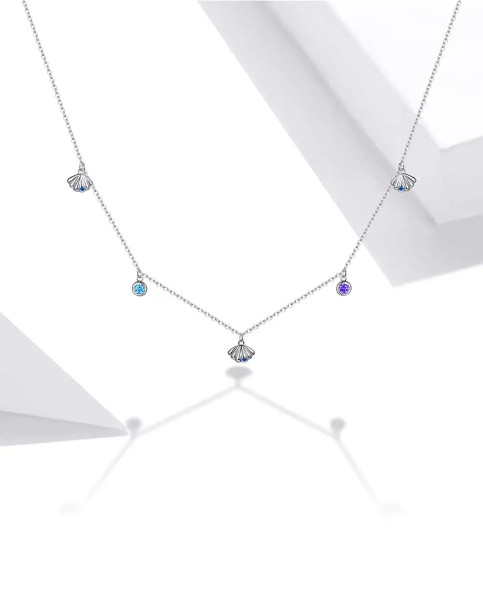 Scallop charm necklace in silver with colorful zircon accents against a minimalist background.