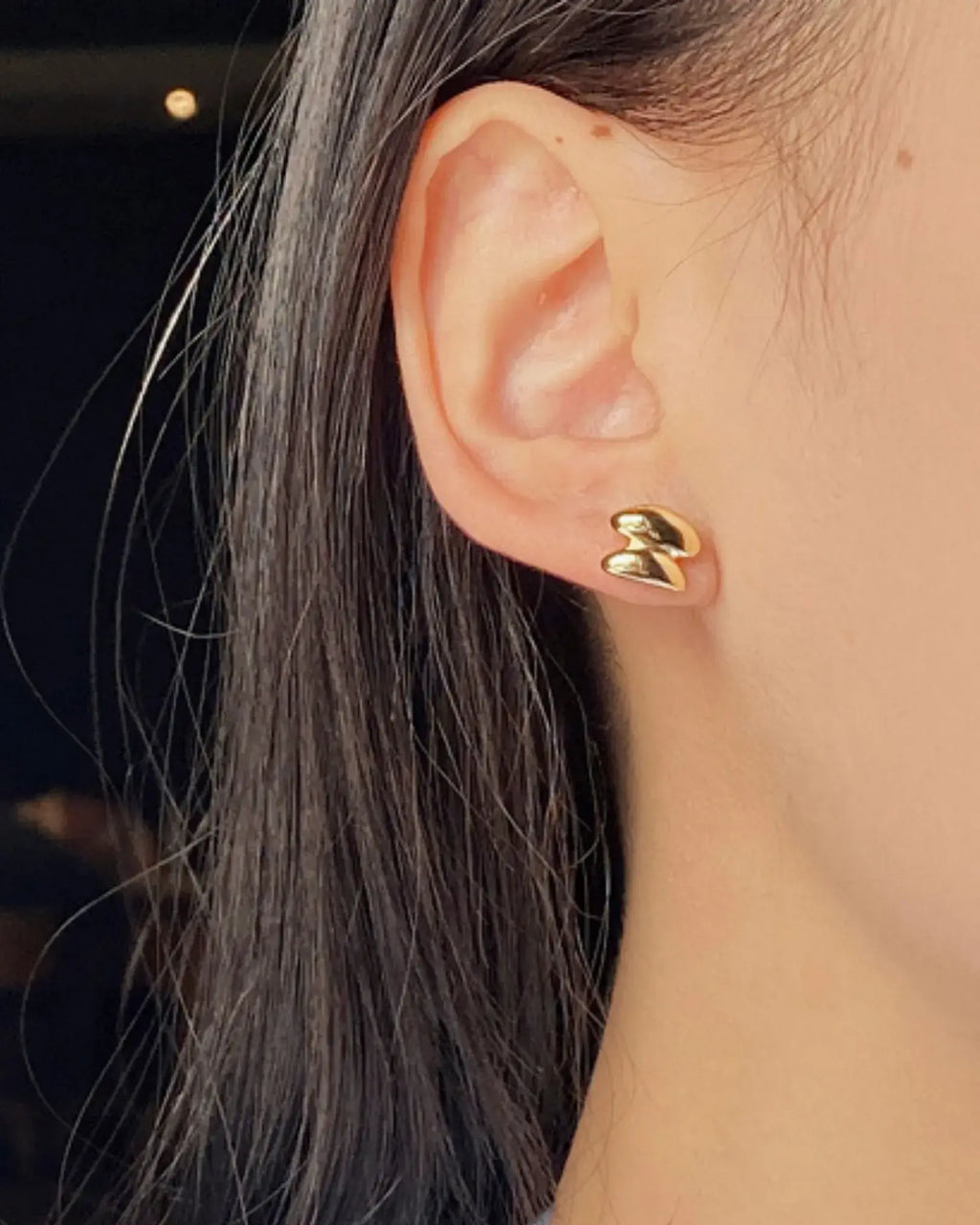 Close-up of a woman wearing Sculptura Ear Studs in 18k gold, showcasing their bold geometric design.