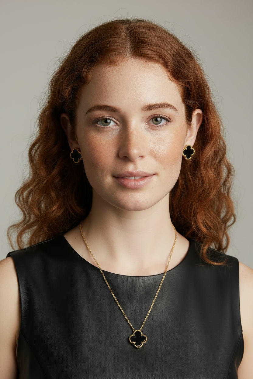 Woman with red hair wearing a black top and gold necklace with clover design.