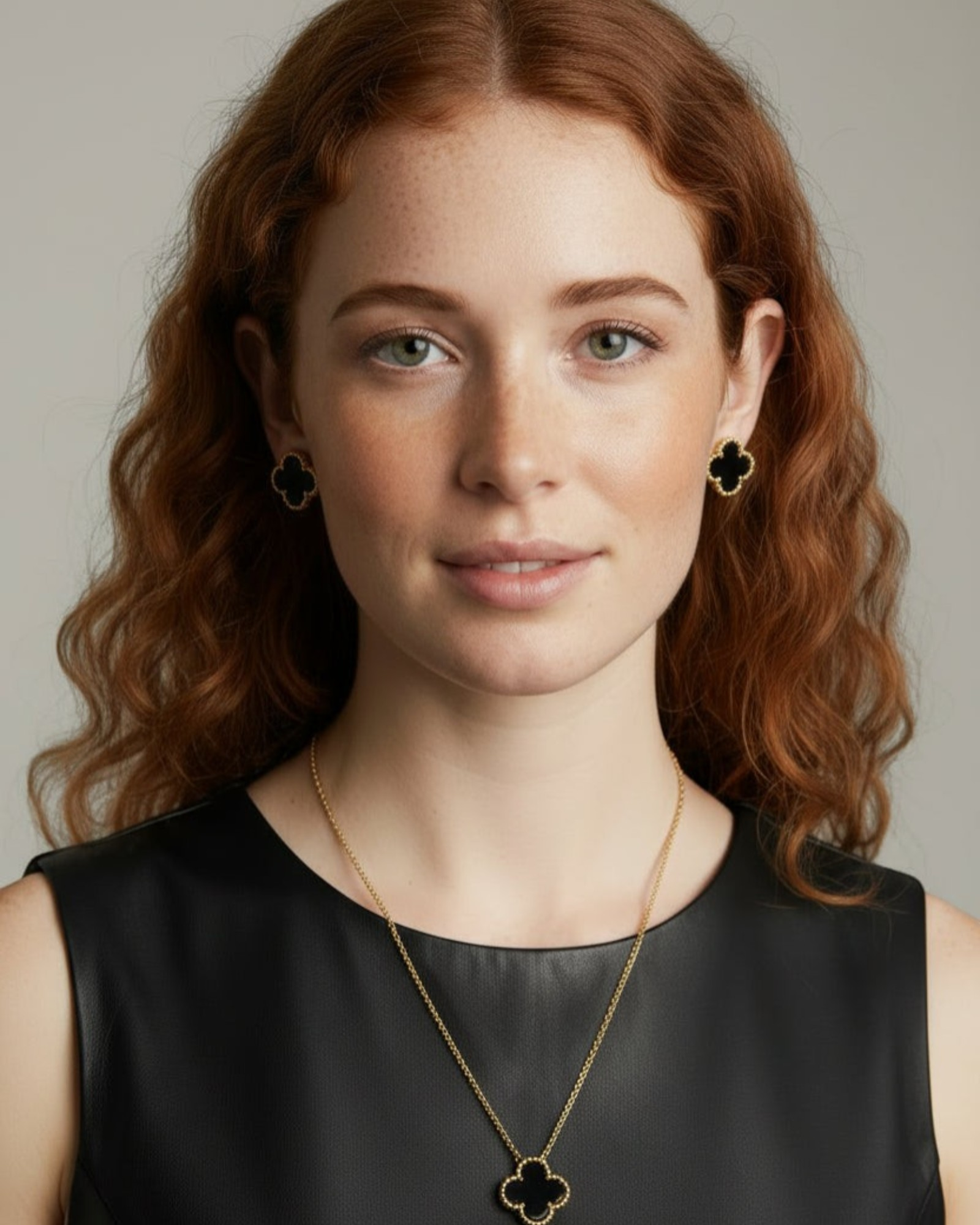 Woman with red hair wearing a black top and gold necklace with clover design.